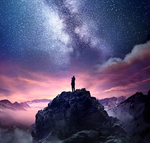 A man standing on a high rock watching the stars rise into the night sky as sun rises